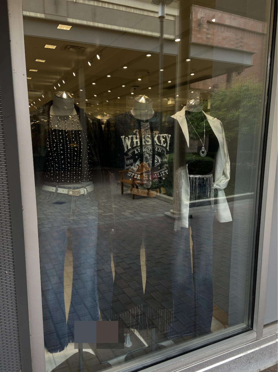 Country outfits on display in the window: Jeans, a whiskey t shirt, and a rhinestone fringe top, all paired with jeans