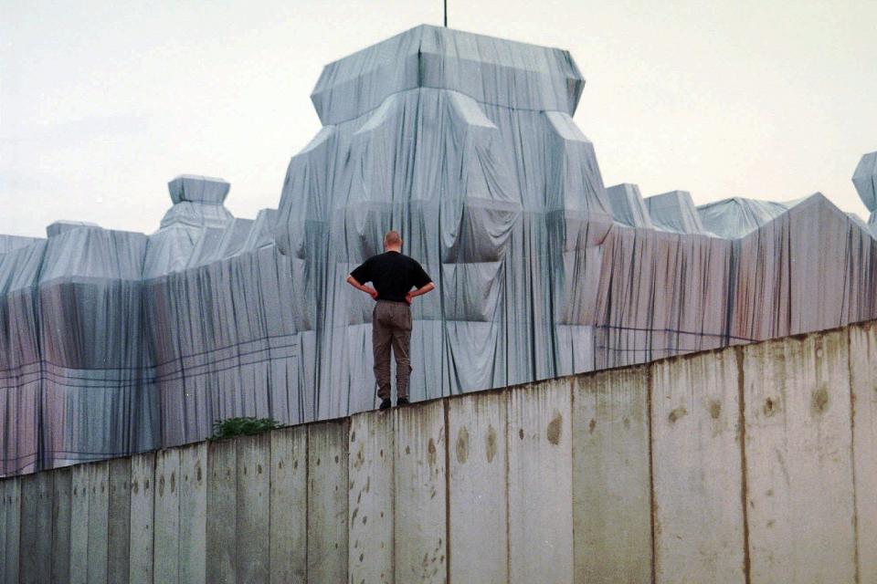 FILE - In this June 22, 1995, file photo, a man stands at the top of remains of the Berlin Wall and looks at the wrapped Reichstag building, a project titled "Wrapped Reichstag" by American artist Christo and his wife Jeanne-Claude. Christo, known for massive, ephemeral public arts projects, has died. His death was announced Sunday, May 31, 2020, on Twitter and the artist's web page. He was 84. Jeanne-Claude died in 2009. (AP Photo/Jan Bauer, File)