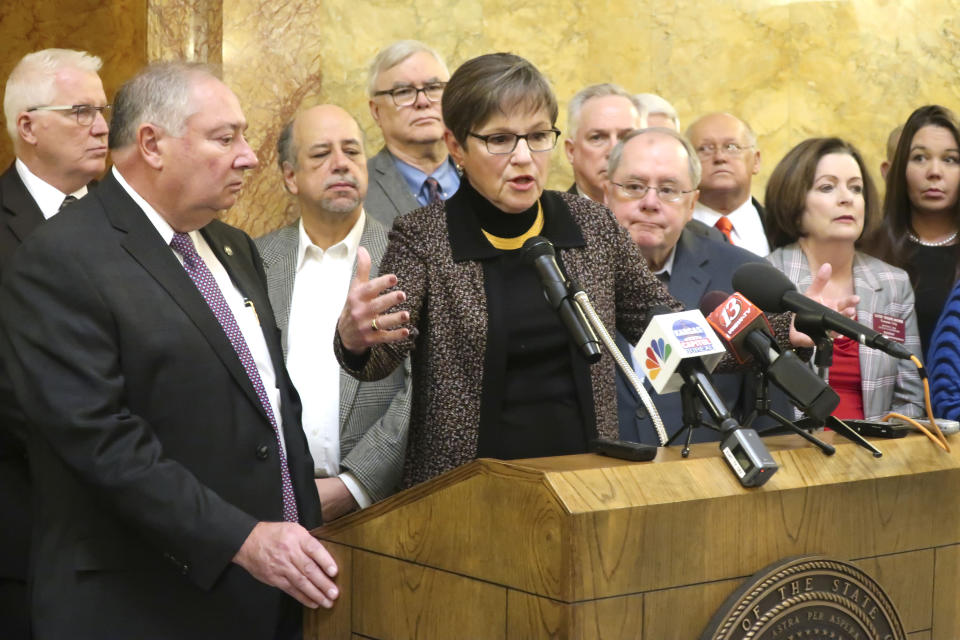 Kansas Gov. Laura Kelly, center, answers questions from reporters about a new Medicaid expansion plan as lawmakers and other advocates watch, including Senate Majority Leader Jim Denning, second from the left, during a news conference, Thursday, Jan. 9, 2020, at the Statehouse in Topeka, Kansas. (AP Photo/John Hanna)