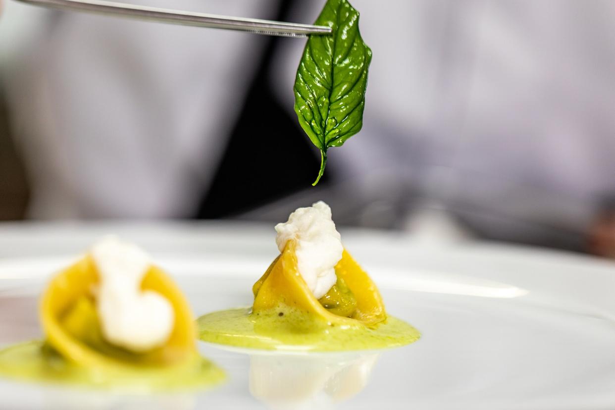 A chef puts a basil leaf on a small, bite-size pasta dish