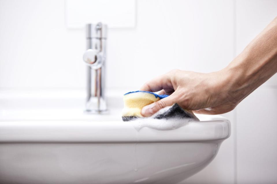 Woman cleaning bathroom sink with sponge