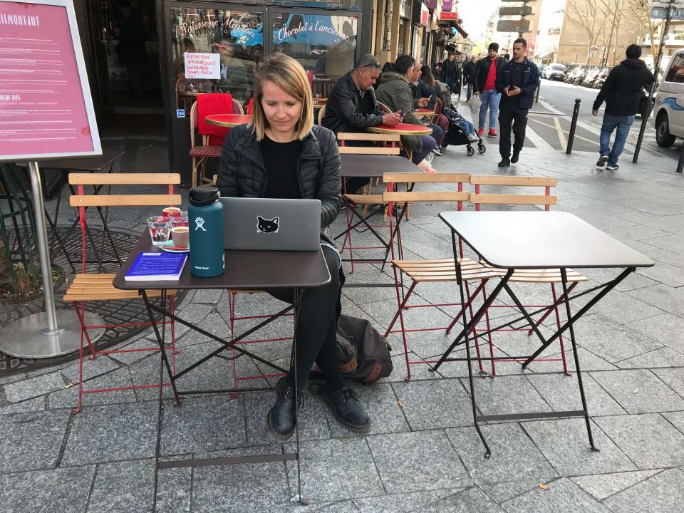 A woman sitting outside at a cafe working on her laptop.