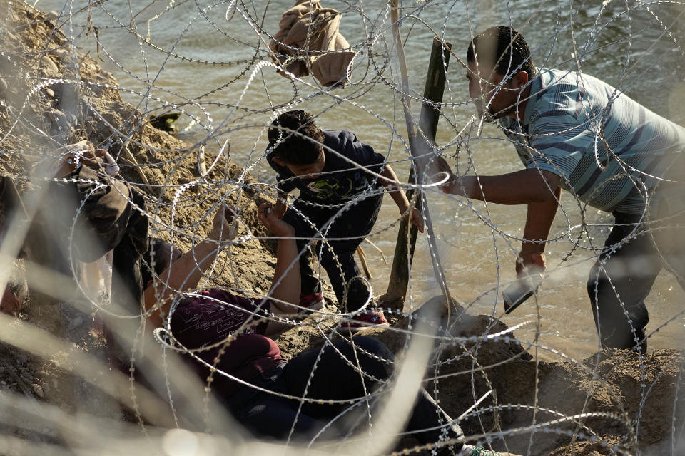 Migrants who crossed the Rio Grande from Mexico to the U.S. work their way through concertina wire, Friday, Sept. 22, 2023, in Eagle Pass, Texas. In March 2023, the U.S. government moved thousands of green card applications for vulnerable minors from Central America in the queue for religious workers, leading to long delays and putting ministers on temporary work visas of losing the ability to stay in the United States. (AP Photo/Eric Gay)
