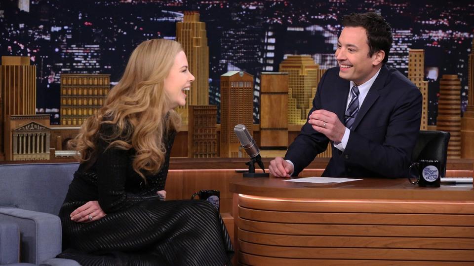 Nicole Kidman in a black dress laughs as she tells a story to Jimmy Fallon behind his desk on "The Tonight Show"