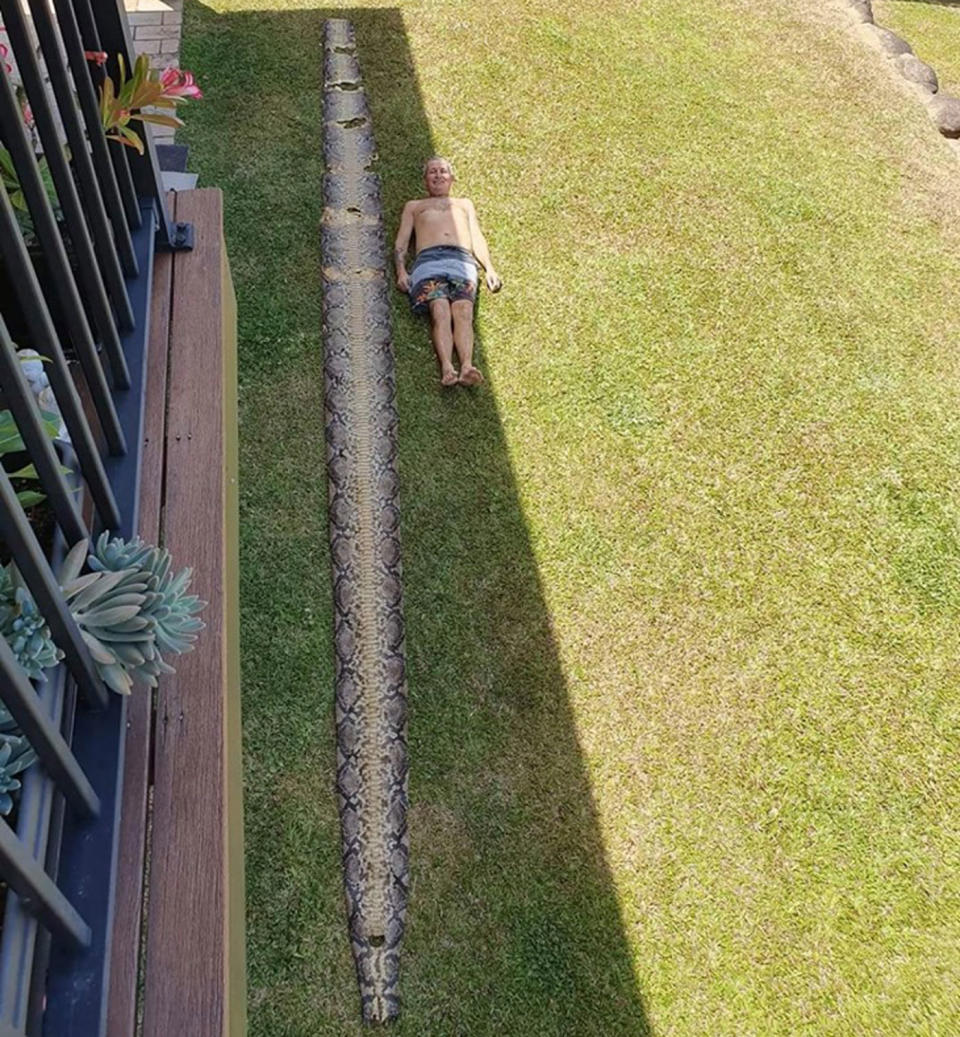 Stuart Morris lays outside a home in Cairns next to a seven-metre snake skin.