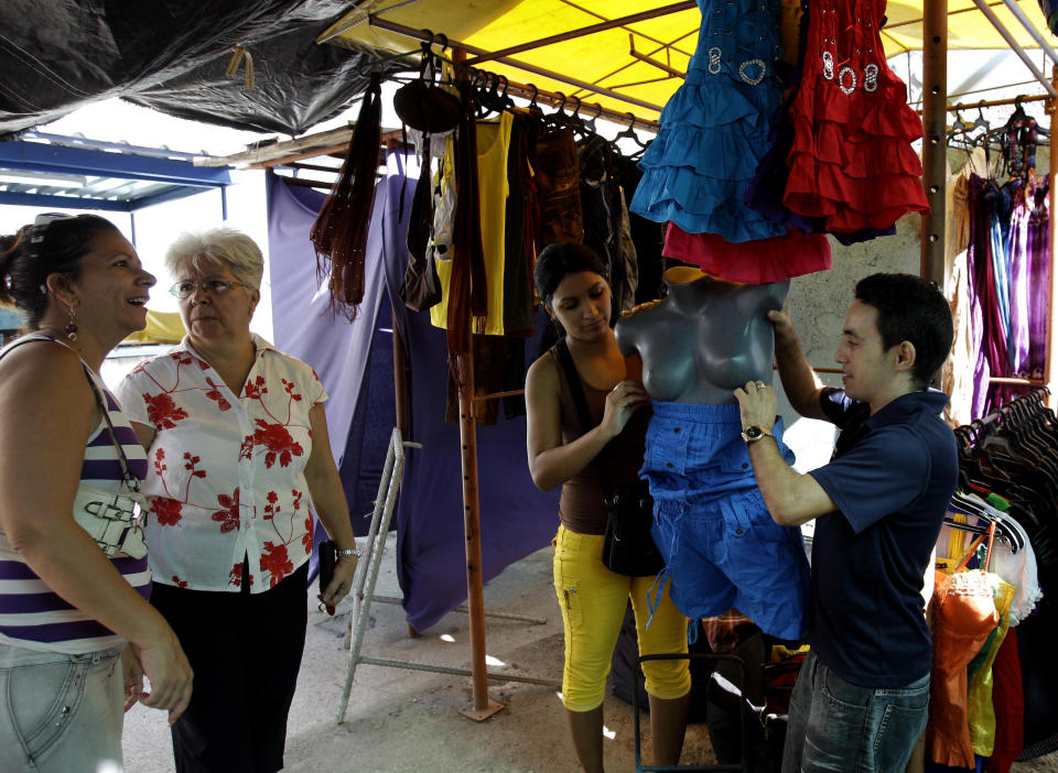 In this Aug 29, 2012 photo, venders Yeisker Castillo and his wife Lisbet Tejeda, right, dress a mannequin at their stall as clients walk through the open-air market where the government allows licensed vendors to sell their goods in downtown Havana, Cuba. A jump in import taxes on Monday, Sept. 3 threatens to make life tougher for some of Cuba's new entrepreneurs who the government has been trying to encourage as it cuts a bloated workforce in the socialist economy. In Cuba, the average monthly wage is about $20. (AP Photo/Franklin Reyes)