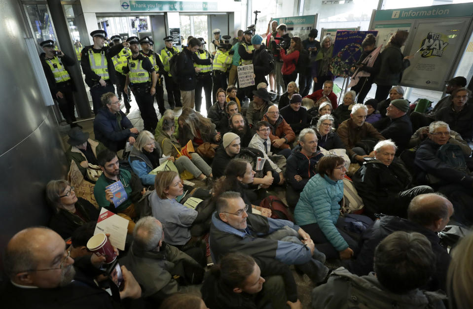 Police Officers stand guard as Extinction Rebellion demonstrators peacefully block an entrance to City Airport in London, Thursday, Oct. 10, 2019. Some hundreds of climate change activists are in London during a fourth day of world protests by the Extinction Rebellion movement to demand more urgent actions to counter global warming. (AP Photo/Matt Dunham)