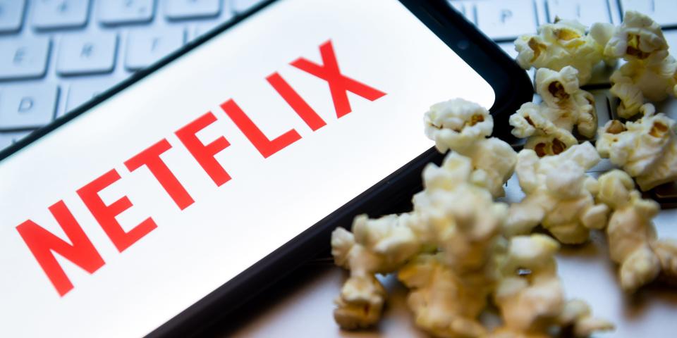 The Netflix logo is displayed on a smartphone with popcorn and laptop keyboard in the background.