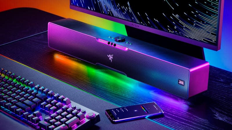 The Razer new Leviathan V2 Pro soundbar on a desk below a computer monitor with its RGB lighting creating a colored rainbow effect.
