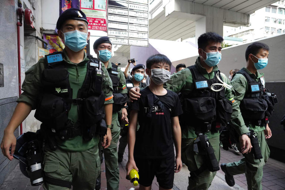 A boy is escorted by police officers to a police van after he walked past the Prince Edward subway station where people tried to place flowers outside and the boy have released soon after, Monday, Aug. 31, 2020 in Hong Kong. Aug. 31 is the first anniversary of police raid on Prince Edward subway station which resulted in widespread images of police beating people and drenching them with pepper spray in subway carriages. (AP Photo/Vincent Yu)