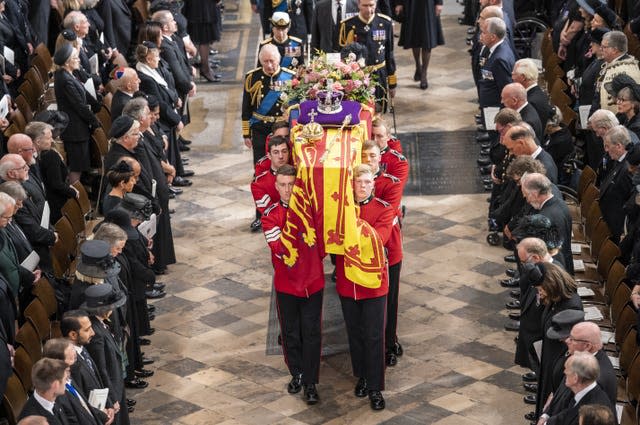 Elizabeth II's coffin, draped in the Royal Standard with the Imperial State Crown and the Sovereign’s orb and sceptre, is carried out of Westminster Abbey after her state funeral, with the King and other members of the royal family walking behind