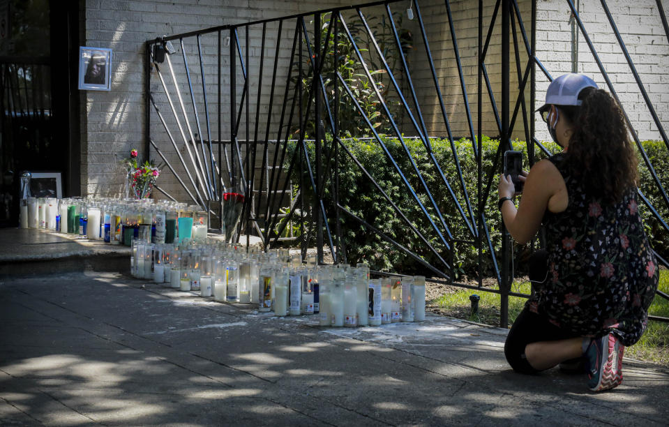 A woman make photos of the memorial scene for shooting victim Deshawn Reid at the entrance to the apartment where he lived, Monday, Aug. 17, 2020, in New York. President Donald Trump is again threatening to send federal agents to New York City if local authorities don't stop a surge of violence that has left seven people dead. Including Reid, 28, and more than 50 people shot since Friday. (AP Photo/Bebeto Matthews)