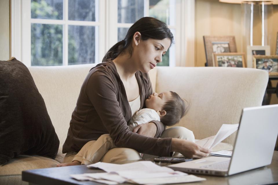 Hispanic woman paying bills online with sleeping baby