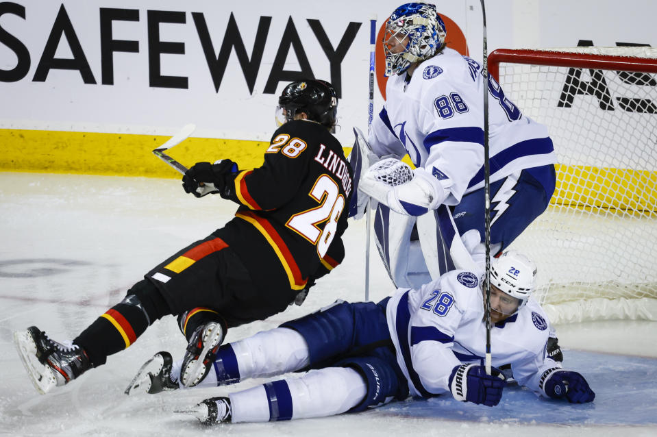 Tampa Bay Lightning defenseman Ian Cole, right, knocks Calgary Flames forward Elias Lindholm to the ice in front of goalie Andrei Vasilevskiy during the second period of an NHL hockey game in Calgary, Alberta, Saturday, Jan. 21, 2023. (Jeff McIntosh/The Canadian Press via AP)