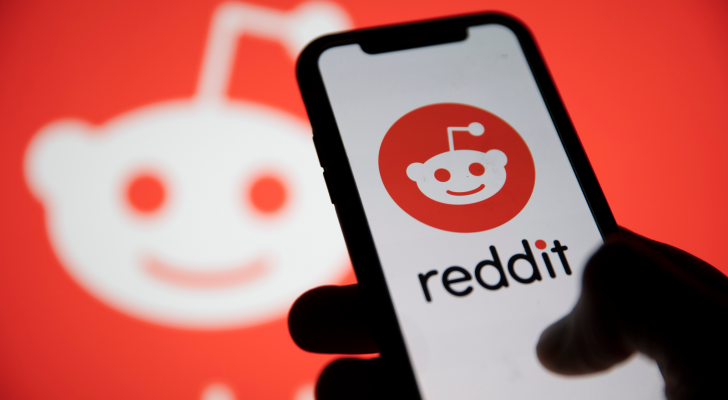 Reddit Layoffs. Phone showing Reddit logo on screen in front of blurred background with reddit logo. Reddit IPO. AI Stocks