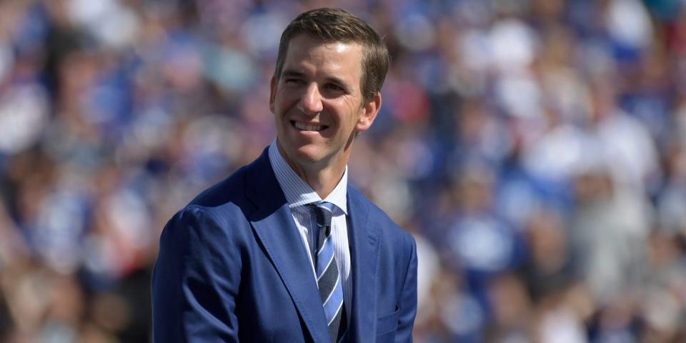 Eli Manning, dressed in a suit, smiles and looks on at his Giants jersey retirement ceremony in 2021.
