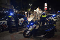 Police officers patrol as people walk on the street in Fuengirola, near Malaga, Spain, Saturday, Aug. 8, 2020. The increase in Spain of coronavirus outbreaks associated with nightlife has set off alarms in recent days, mainly in tourist areas where pubs and discos are full before the summer tourist campaign. (AP Photo/Jesus Merida)