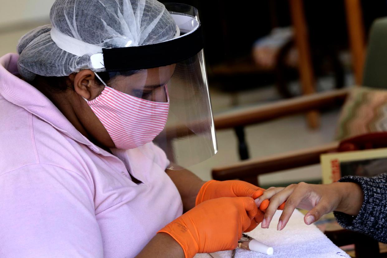 A manicurist wears a mask, face shield and gloves as protection against the COVID-19 pandemic while attending a client on the first day the saloon was allowed to reopen as restrictions ease in Brasilia, Brazil on Wednesday, July 15, 2020.