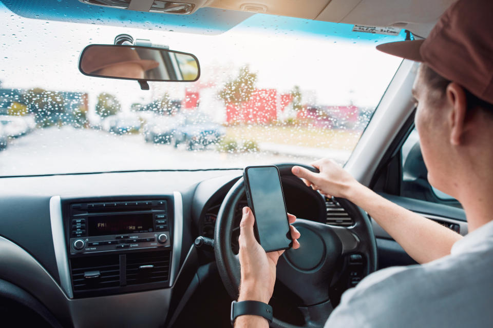 An Uber driver looks at his phone while in the driver's seat.