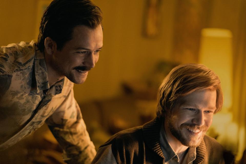 a still from the film tetris, with actors taron egerton and nikita efremov looking down at something off screen and smiling