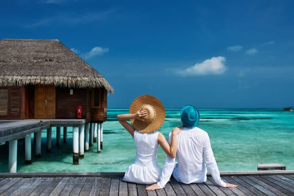 Vacationing couple seated on a beach jetty in the Maldive Islands.