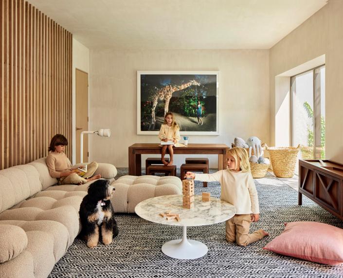 Brooks, 10, Scarlett, 7, Grey, 5, and Ruby the bernedoodle play in style thanks to a Mario Bellini sofa and a kid-size table and benches that were custom-made by Shepard Design Co in East Hampton. The area rug was custom-made by <a href="https://www.saccocarpet.com/" rel="nofollow noopener" target="_blank" data-ylk="slk:Sacco Carpet" class="link ">Sacco Carpet</a> and the marble coffee table is vintage Eero Saarinen.