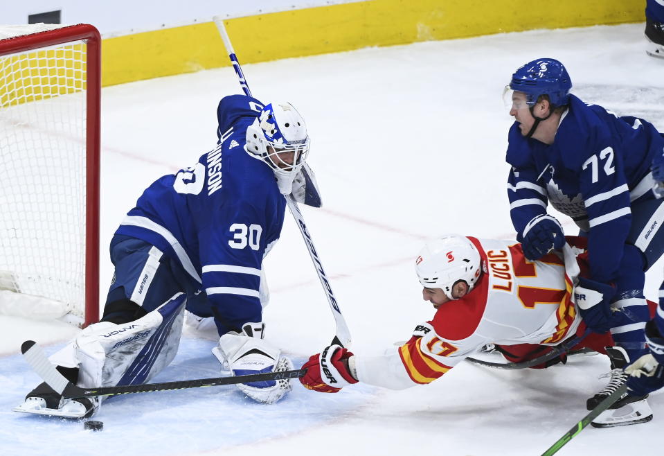 Toronto Maple Leafs goaltender Michael Hutchinson (30) makes a save against Calgary Flames left wing Milan Lucic (17) as Maple Leafs center Travis Boyd (72) gets a penalty on the play during second-period NHL hockey game action in Toronto, Monday, Feb. 22, 2021. (Nathan Denette/The Canadian Press via AP)