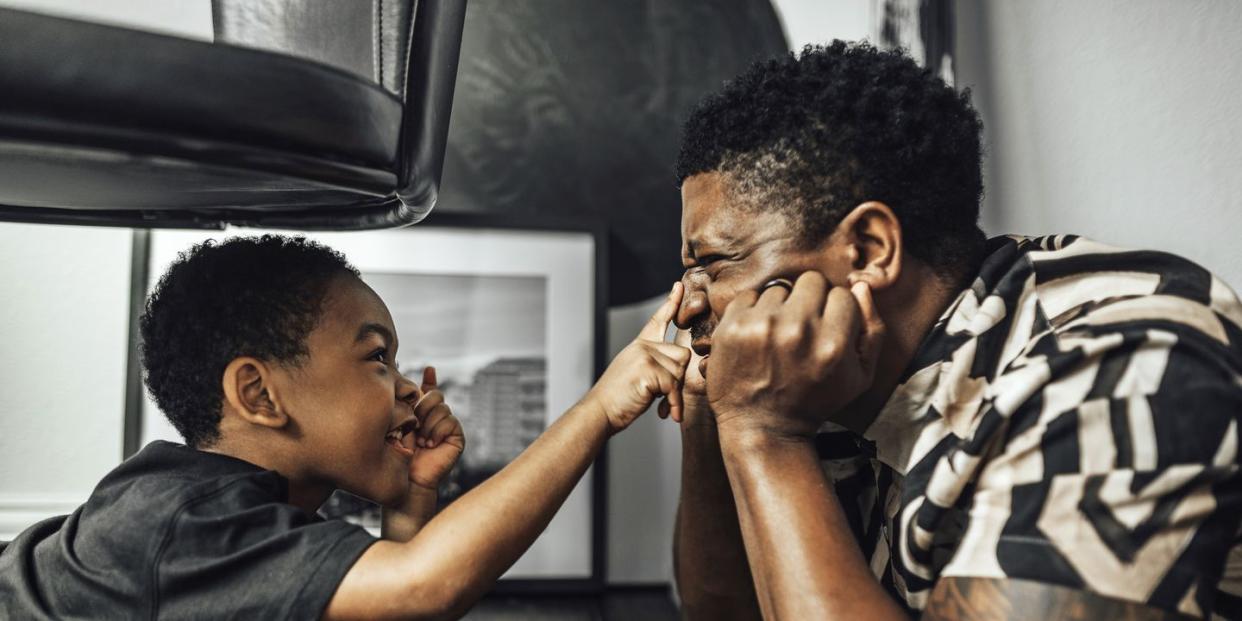 father and son playing on the floor under a chair son reaches over and touches fathers nose