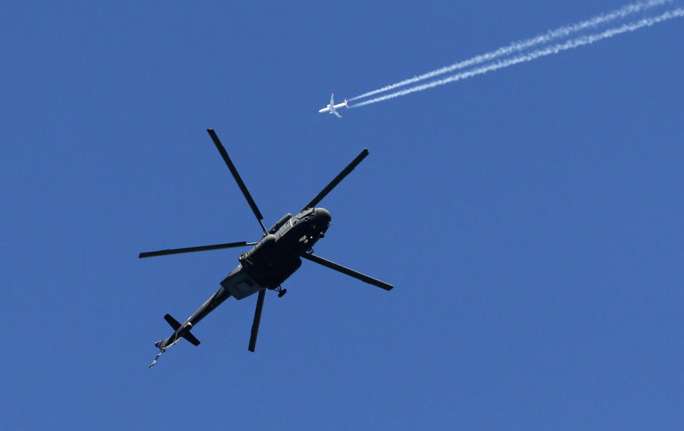 A military helicopter hovers over the mountain cluster as a passenger jet passes by prior to the 2014 Winter Olympics, Tuesday, Feb. 4, 2014, in Krasnaya Polyana, Russia. With militant groups threatening to attack during the next few weeks, security and the safety of competitors and visitors to the coastal area and in the nearby mountains that will host the events has become both heightened and inescapable. (AP Photo/Dmitry Lovetsky)