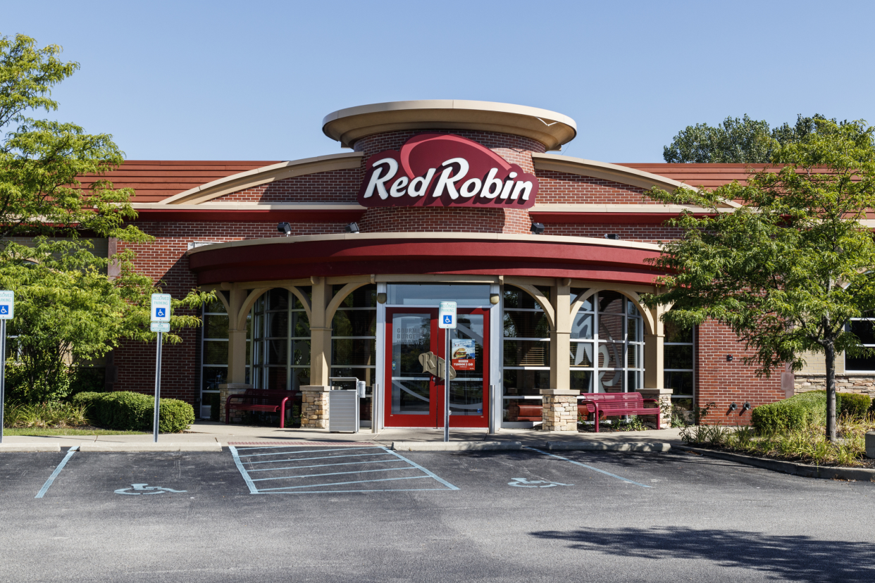 Front exterior of a Red Robin gourmet burgers and brews restaurant in Carmel, Indiana, front doors and handicapped parking spots surrounded by trees and shrubbery with a blue sky in the background