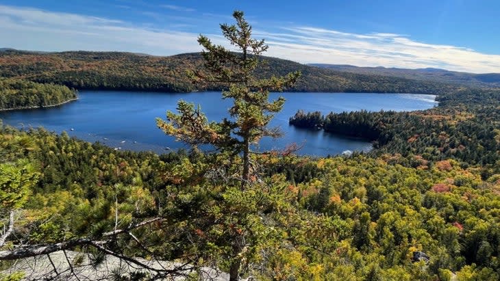 A clifftop view of a cobalt-blue Debsconeag Lake surrounded by the forest