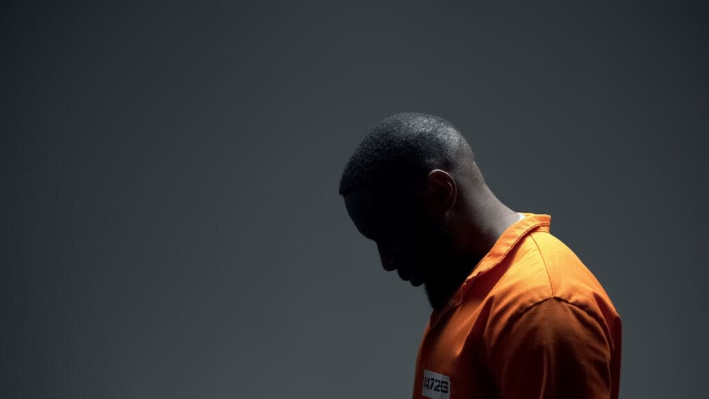 Black man in orange jumpsuit in prison