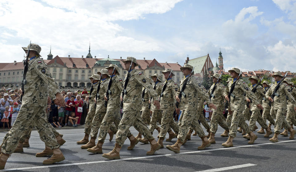 Polish Army soldiers salute as tanks roll on one of the city's main streets during a yearly military parade celebrating the Polish Army Day in Warsaw, Poland, Wednesday, Aug. 15, 2018. Poland marks Army Day with a parade and a call for US permanent military base in Poland. (AP Photo/Alik Keplicz)
