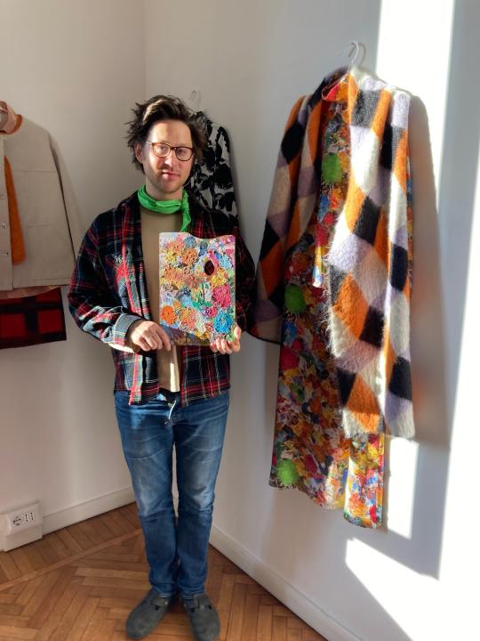 Milan-based Austrian fashion designer Arthur Arbesser, poses in his studio holding a painter’s pallet that he picked up at a flea market, and which inspired the signature print for his Fall 2021 collection of 25 looks, in Milan, Italy, Sunday, Feb. 28, 2021. Arbesser decided against a runway show in this digital era, instead focusing his creative energies to make a collection from revitalized textiles from his archives that he had printed over, and experimenting with other artisanal techniques with his small team. (AP Photo/Colleen Barry)