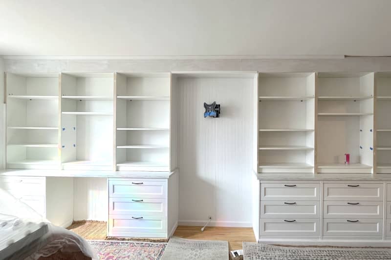 White wooden shelving and drawers go up along wall.