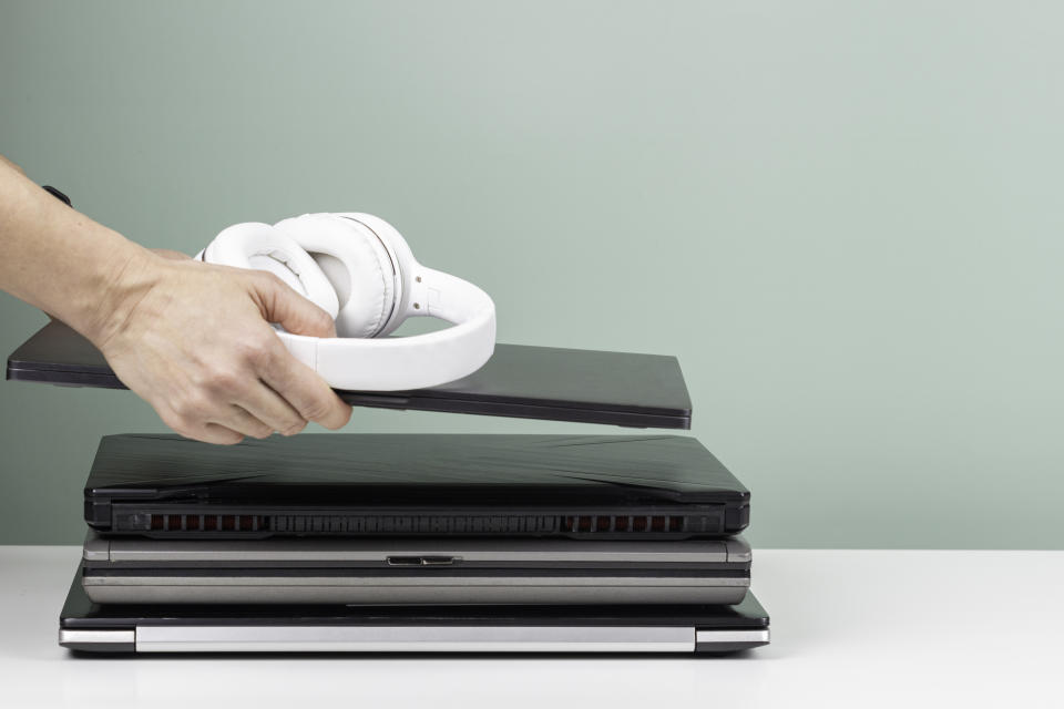 Woman hands put laptop computer and headphones on pile of old used laptop computers for recycling on white table. Planned obsolescence, e-waste, electronic waste for reuse and recycle concept.