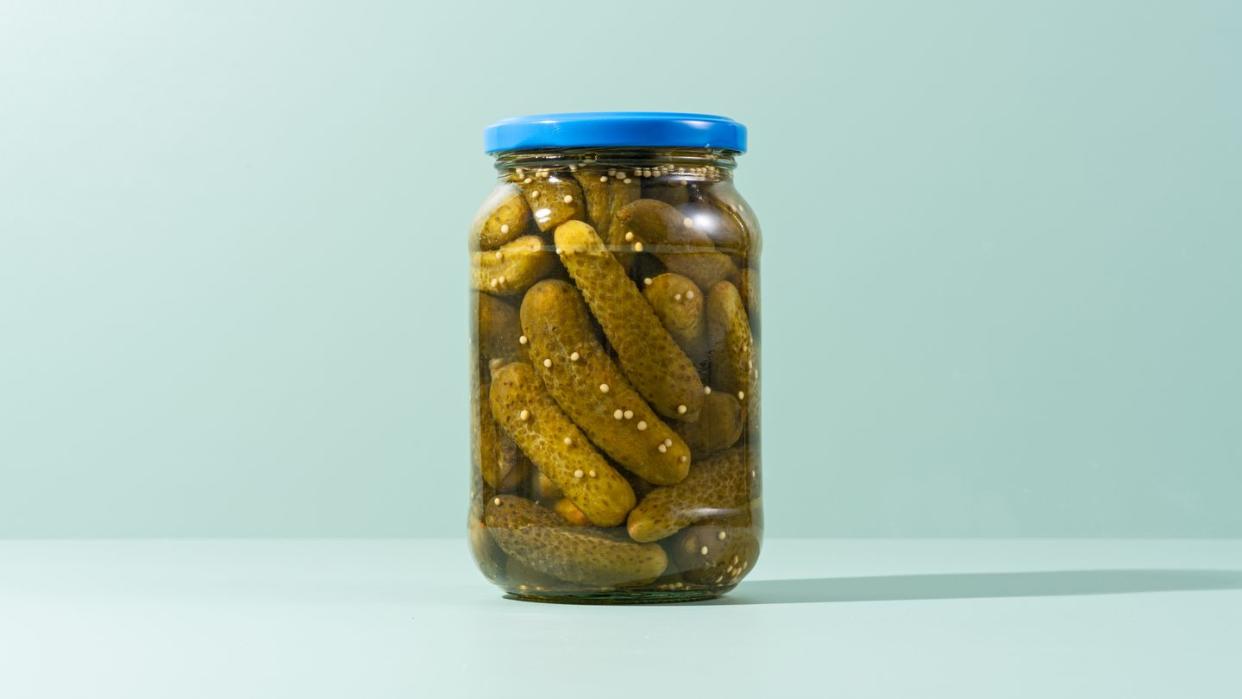 pickles, preserved gherkins in glass jar on green background