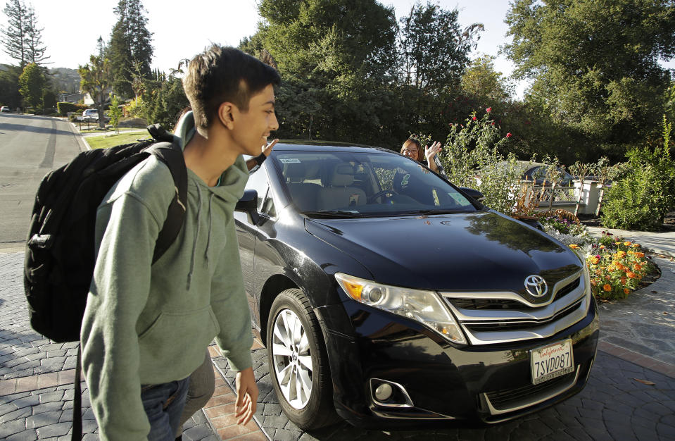 In this photo taken Tuesday, Oct. 29, 2019, Zum driver Stacey Patrick, right, waves goodbye to student Saahas Kohli, left, and his mother, Alpa Kohli, obscured behind her son, as he returns home from school in Saratoga, Calif. A handful of ride-hailing companies have surfaced that allow parents to order rides, and in some cases childcare, for children using smartphone apps. The promise is alluring at a time when children are expected to accomplish a dizzying array of extracurricular activities and the boundaries between work and home have blurred. But the companies face hurdles convincing parents that a stranger hired by a ride-hailing company is trustworthy enough to ferry their most precious passengers. (AP Photo/Ben Margot)