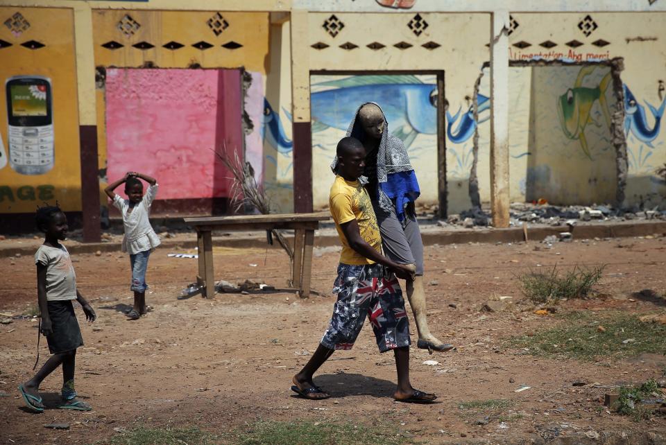 A Christian man carries a charred mannequin wearing a Muslim veil in front of looted Muslim stores, past a convoy of over 100 vehicles of Muslims fleeing Bangui, Central African Republic, Friday Feb. 14, 2014. A convoy of thousands of Muslims heading to Chad had to turn around as MISCA troops, the African force deployed in the Central African Republic, deemed the road out was not secure. (AP Photo/Jerome Delay)