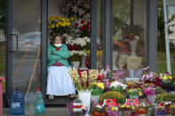 A flower vendor with a mask for protection against the COVID-19 infection, partially covering her face watches people passing by in Bucharest, Romania, Friday, Sept. 18, 2020. (AP Photo/Andreea Alexandru)