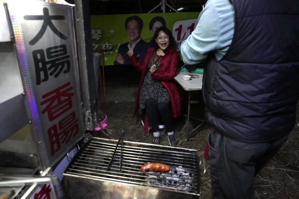 A supporter of the Democratic Progressive Party presidential candidate Lai Ching-te, who also goes by William, poses for photos next to his poster as she eats sausages after a rally in southern Taiwan's Tainan city on Friday, Jan. 12, 2024 ahead of the presidential election on Saturday. (AP Photo/Ng Han Guan)