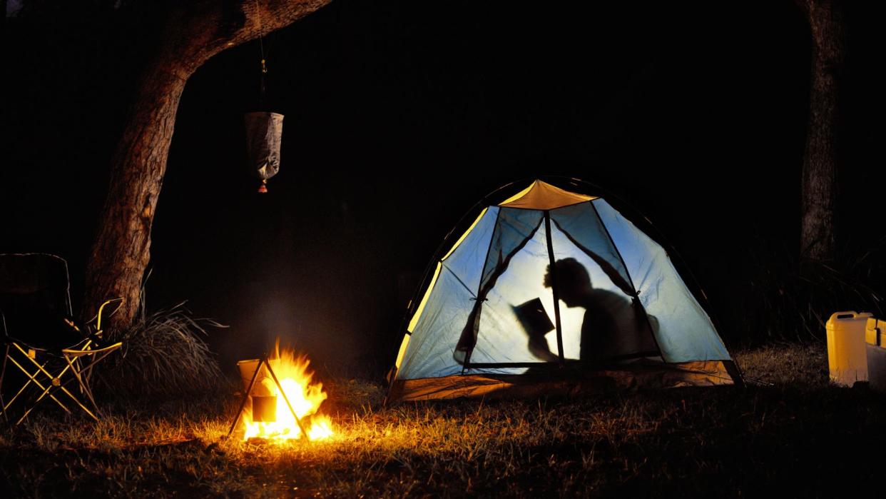  A person sitting in their tent reading a book with a torch. 