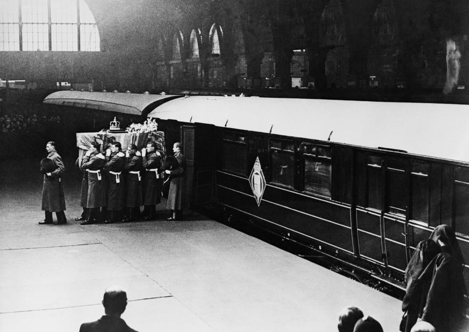 (Original Caption) 2/12/1952-London, England: Guardsmen pallbearers are carrying te coffin of King George VI from the train that bore it from Sandringham to London. The coffin is draped with the Royal Standard on which rest the crown and a single spray of flowers from the widowed Queen. In right foreground are the three mourning Queens, young Queen Elizabeth, daughter; Queen Mother Elizabeth, Widow, and Dower Queen Mary, mother.