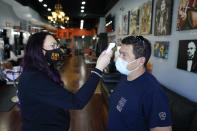 Rudy Pulido has his temperature checked by Melissa Acosta before he had his hair cut at Orange County Barbers Parlor on Wednesday, July 15, 2020, in Huntington Beach, Calif. Gov. Gavin Newsom ordered that indoor businesses like salons, barber shops, restaurants, movie theaters, museums and others close due to the spread of COVID-19. (AP Photo/Ashley Landis)