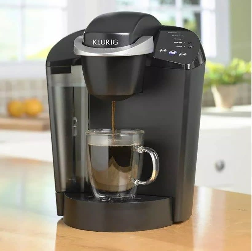 Keurig coffee maker brewing into a clear mug on a kitchen counter