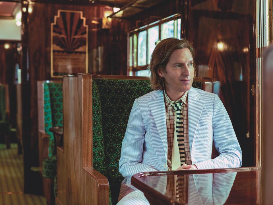 Wes Anderson looking away from the camera as he sits in the Cygnus carriage