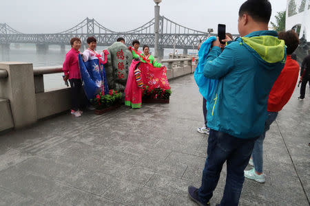 Chinese tourists wearing traditional Korean costumes pose for pictures by the Yalu river, which separates North Korea and China, in Dandong, Liaoning province, China June 7, 2018. REUTERS/Brenda Goh