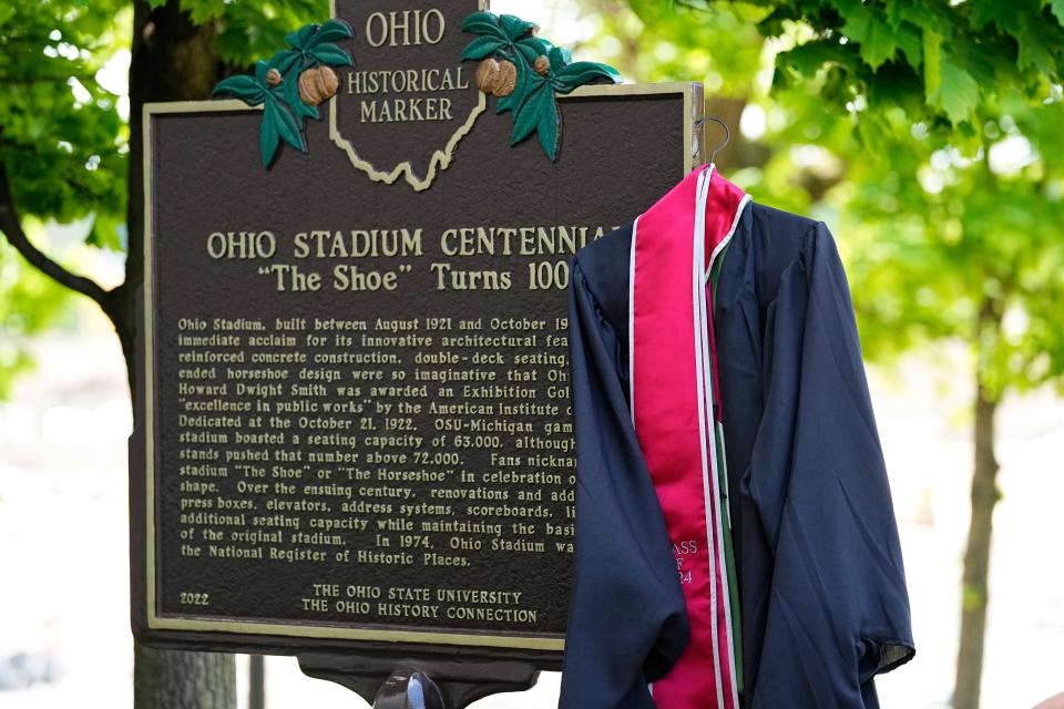 A gown and stole hang on the Ohio Stadium historical marker as Ohio State seniors line up to take photos ahead of Sunday’s commencement ceremony there. Approximately 12,000 are expected to receive their degrees.