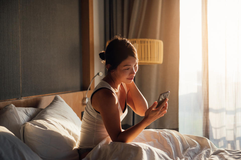 Woman in bed checking phone, early morning light, concept of remote work or checking work messages from home