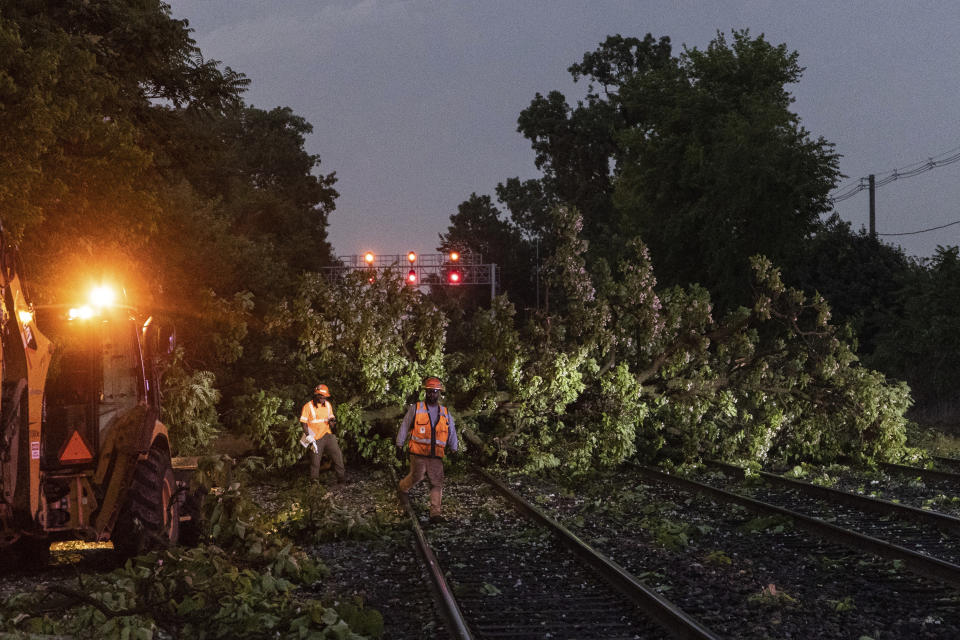 Workers begin to remove fallen trees across the BNSF tracks which stopped train traffic in Riverside Monday, June 13, 2022, from a storm that raced across the Chicago area. A supercell thunderstorm with winds in excess of 80 mph (129 kph) toppled trees and damaged power lines Monday evening as it left a trail of damage across the Chicago area and into northwestern Indiana, the National Weather Service said. (Steven Rosenberg/Chicago Tribune via AP)